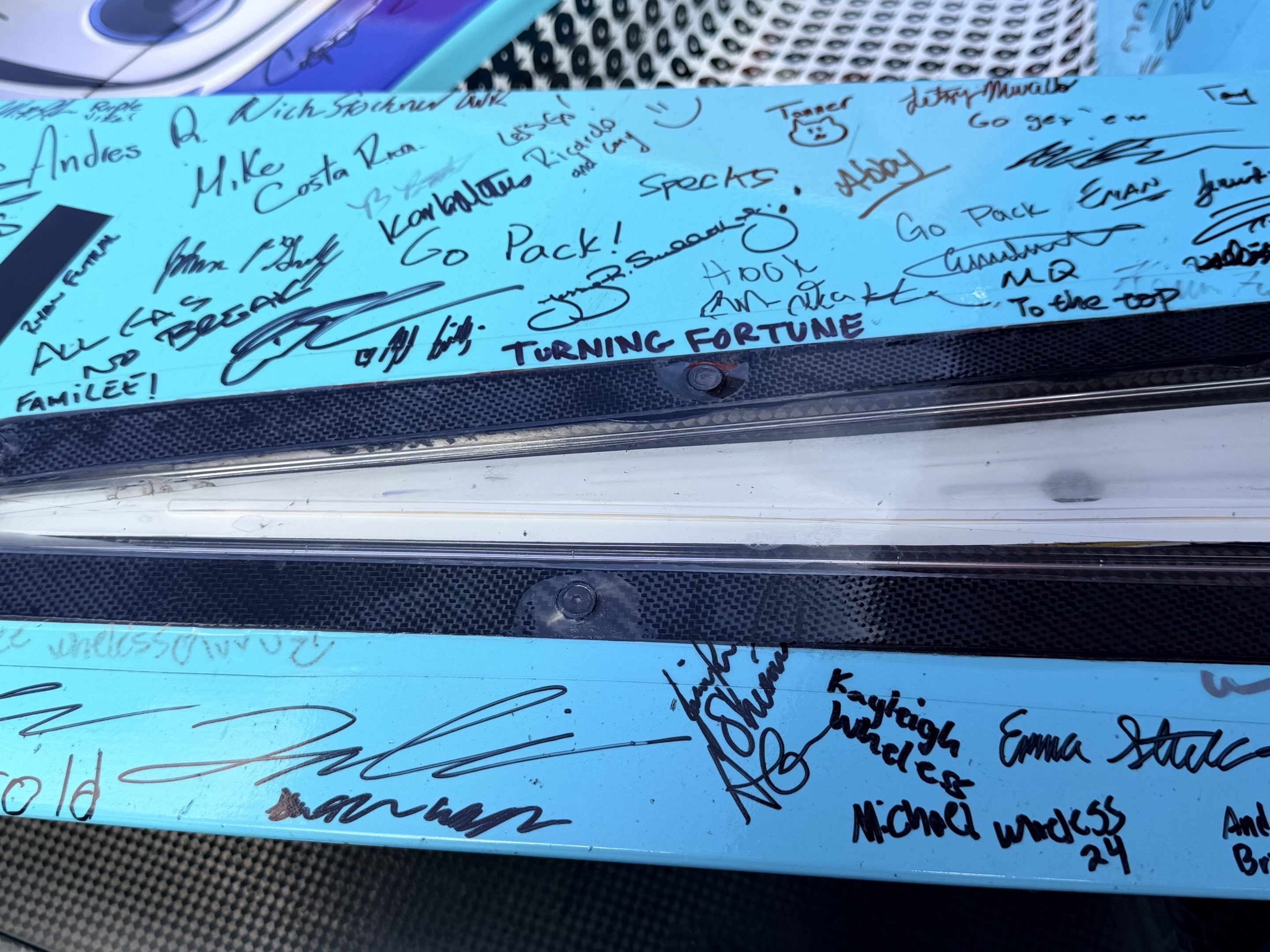 The blue front clip of a race car covered in signatures, one of which says TURNING FORTUNE